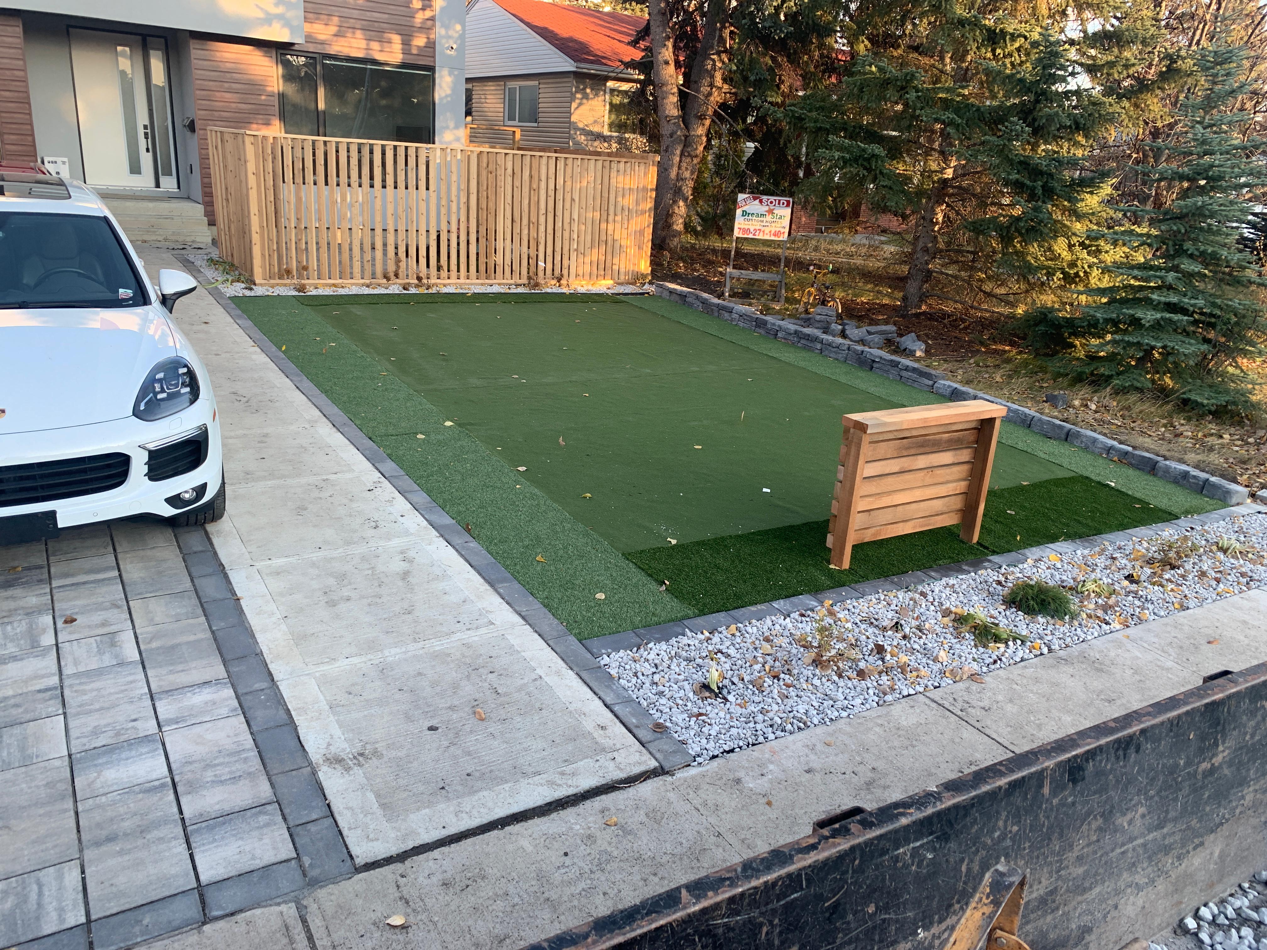 Artificial turf putting green with paver driveway and cedar fence in Edmonton backyard